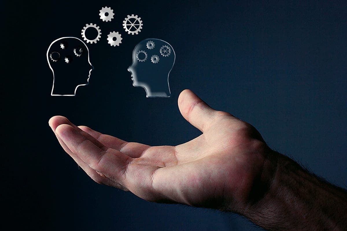 A hand holding an illustration of two minds and gears